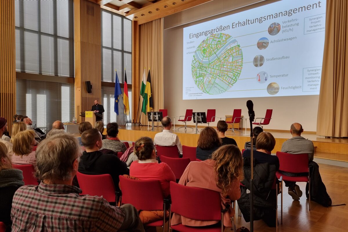 Mann steht auf einer Bühne vor einem sitzenden Publikum