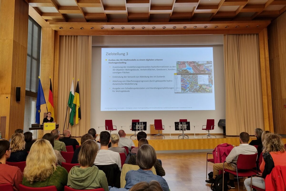 Mann steht auf einer Bühne vor einem sitzenden Publikum