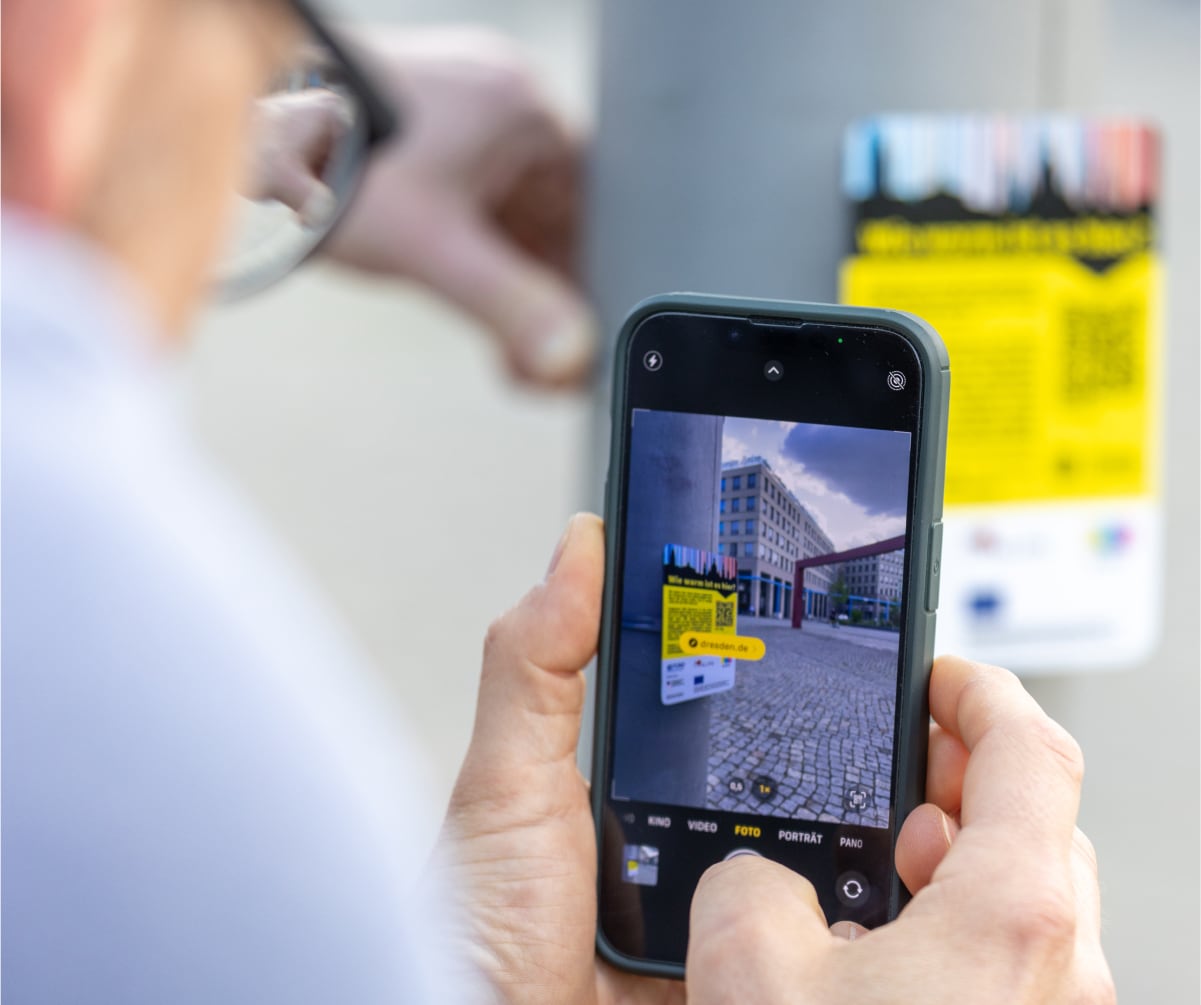 Mann scannt mit Smartphone QR-Code auf Hinweistafel zu Hitzesensoren