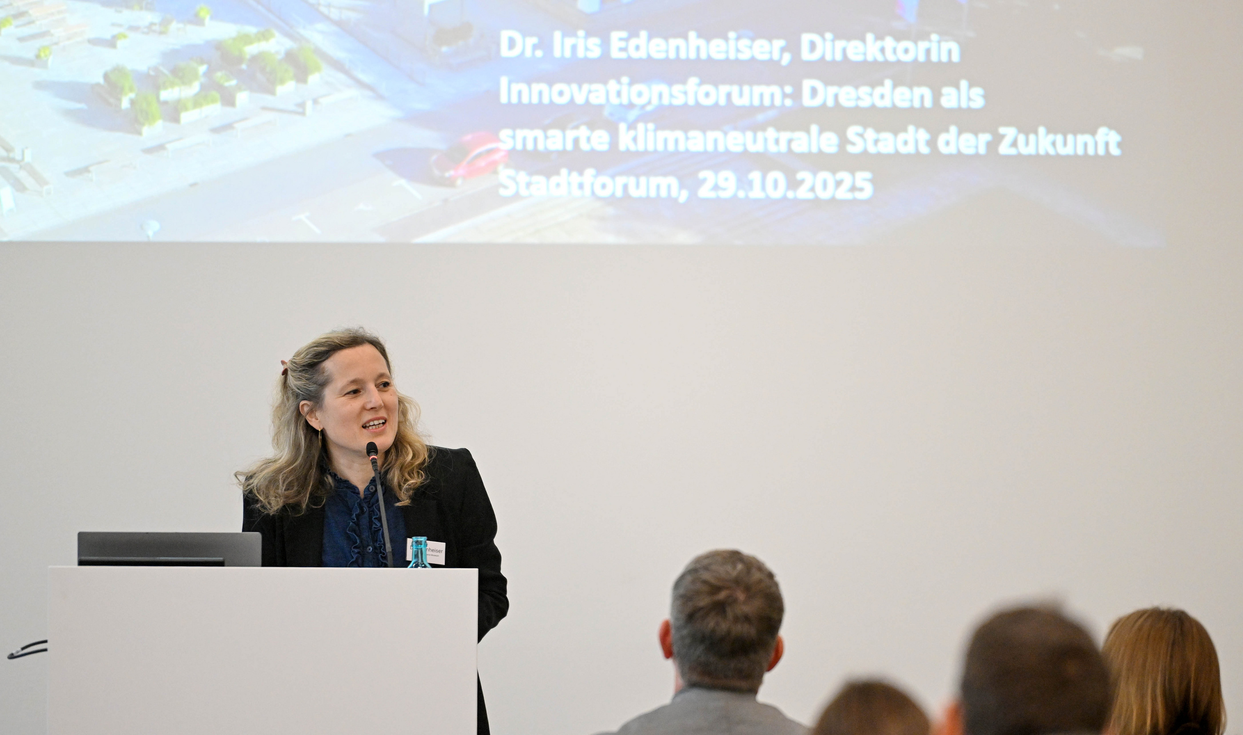 Frau steht an einem Rednerpult vor sitzendem Publikum