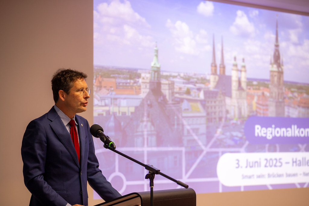 Ein Mann steht an einem Rednerpult mit einer Präsentation im Hintergrund
