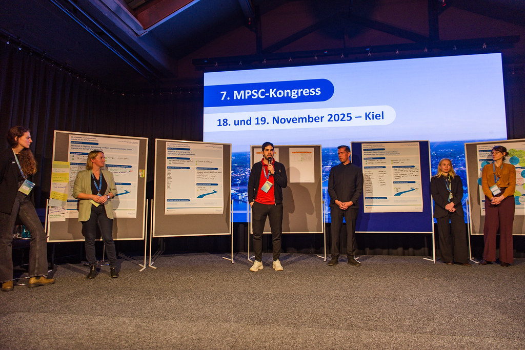 Presentation on stage, six speakers at the front, flipcharts in the background