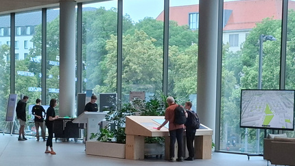 Menschen schauen auf mehrere große Bildschirme, die vor einer großen Glasfront stehen