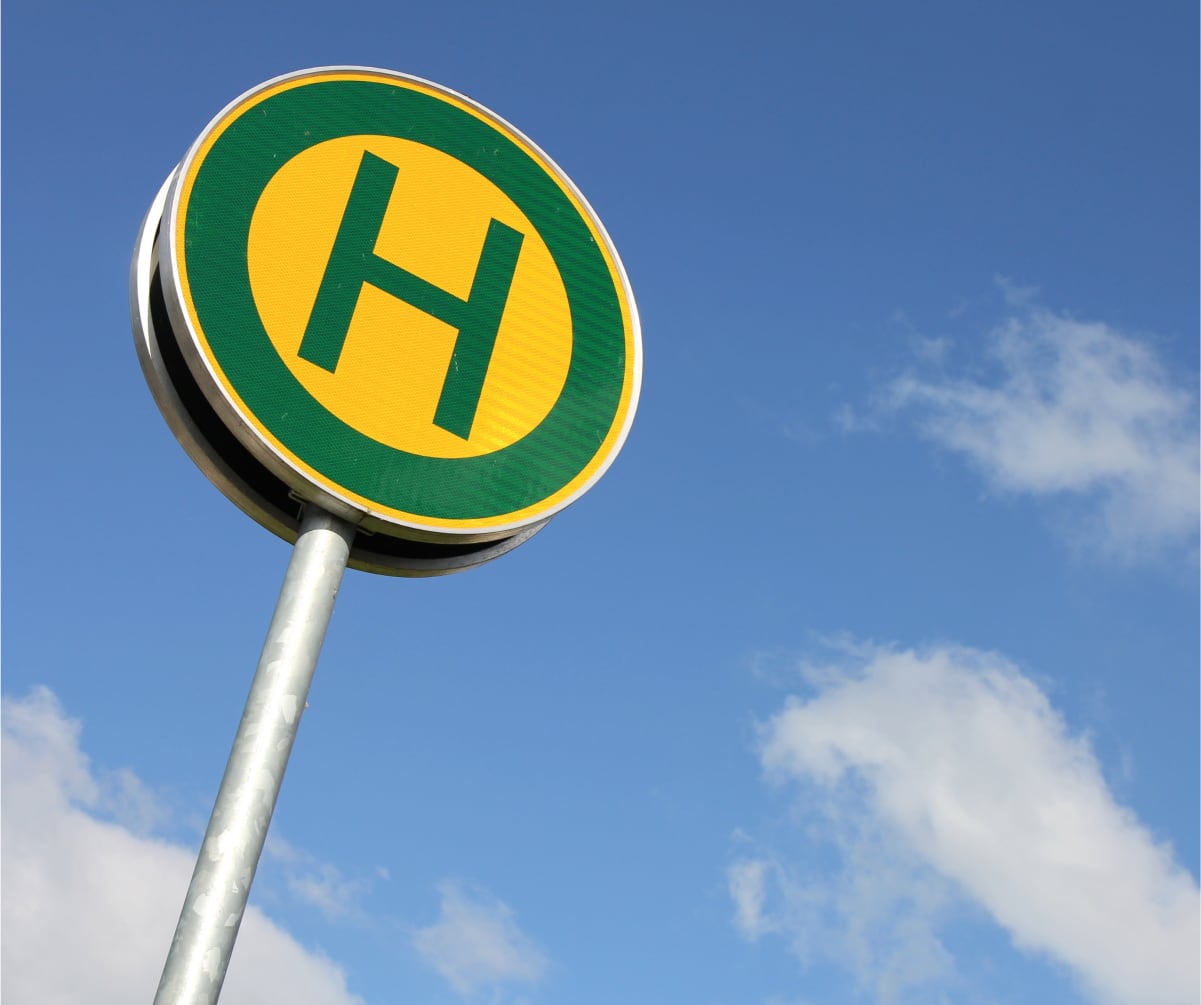 Gelb-grünes Haltestellenschild vor blauem Himmel