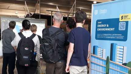 Visitors stand in front of a screen. On the right, a roll-up of the Smart City project.
